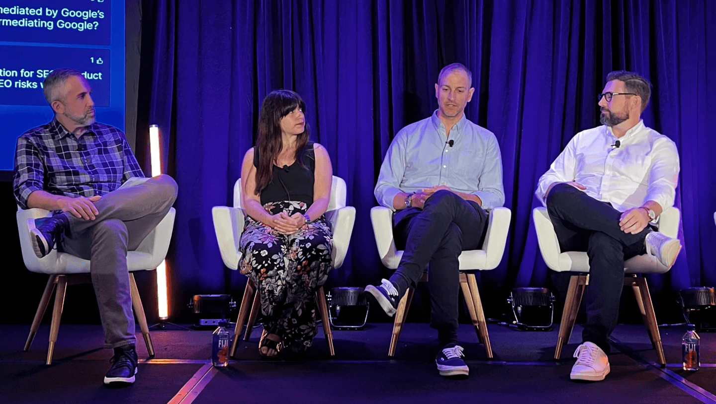 Four panelists seated on stage in front of a screen showing audience questions